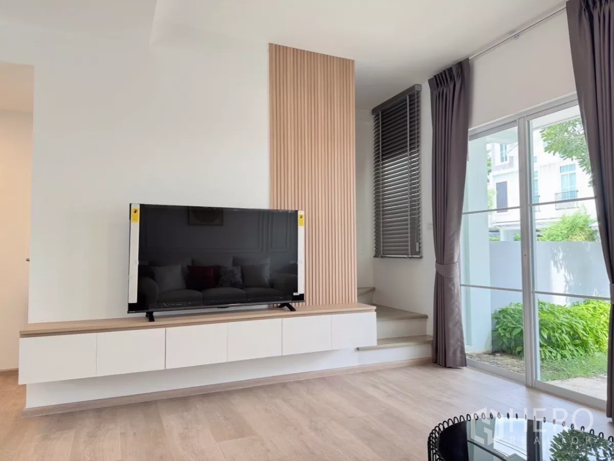 联排别墅 出租在Prawet, Bangkok - 电视墙带竖向木饰面，推拉落地玻璃门通向后花园。