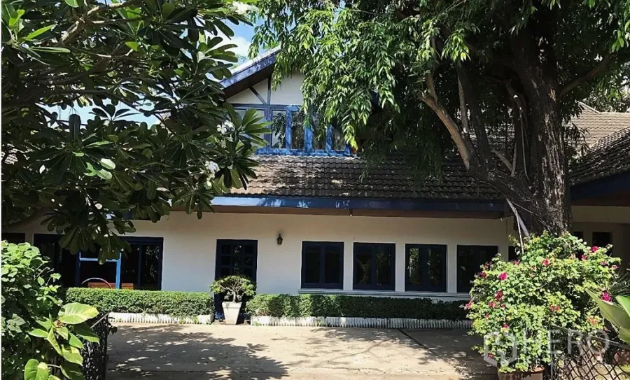 Detached House for rent in Khlong Toei, Bangkok - Shaded exterior of a detached house with gabled roof, blue-trim windows, and mature trees.