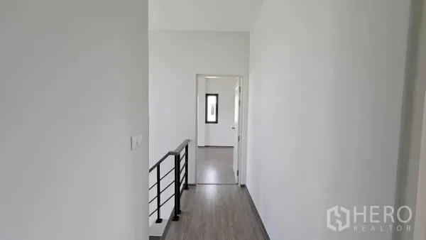Detached House for sale in Samut Prakan - Bright upper-floor hallway with wood-look flooring and black metal railing leading to bedrooms.
