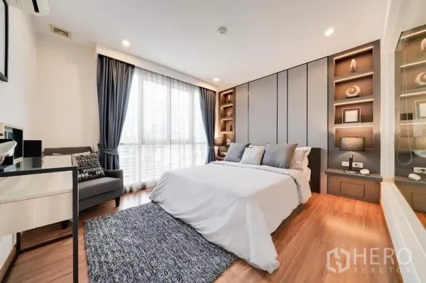 Condominium for sale in Bang Rak, Bangkok - Master bedroom with floor-to-ceiling window, built-in wardrobes and shelving, and warm wood flooring.
