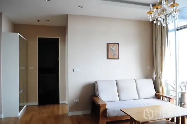Condominium for rent in Pathum Wan, Bangkok - Bright living room with sofa, crystal chandelier, wood floors and large glass wall.