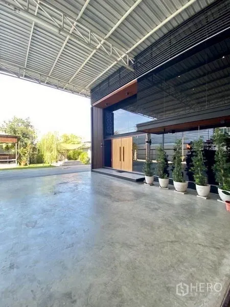 Warehouse for sale in Min Buri, Bangkok - Spacious concrete forecourt and sleek glass office frontage lined with potted plants.