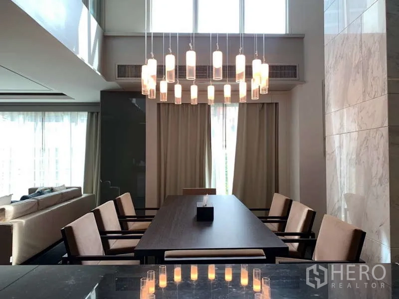 Condominium for rent in Khlong Toei, Bangkok - Dining area for eight beneath a statement chandelier and double-height windows.