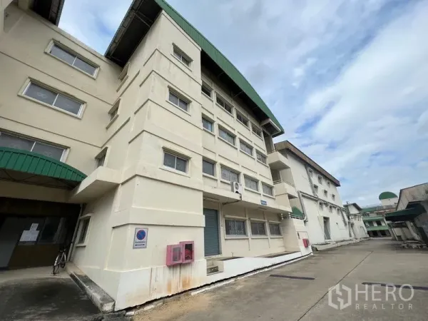 货栈 出租在Bang Kapi, Bangkok - 工业建筑主立面，绿色雨篷与卡车通行的服务通道。