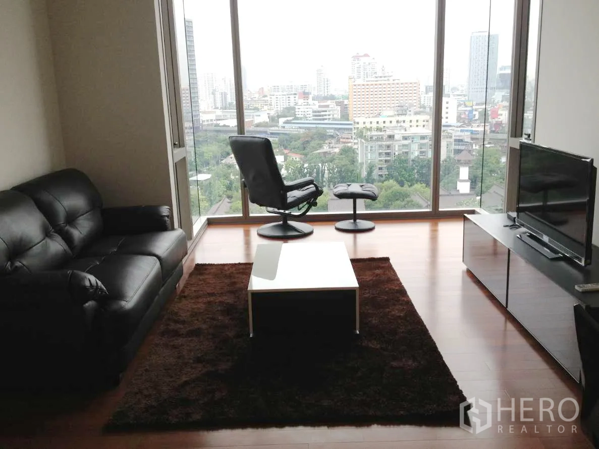 Condominium for rent in Khlong Toei, Bangkok - Living room with leather sofa, TV console and full-height windows overlooking Bangkok skyline.