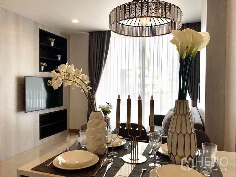 คอนโด ให้เช่าในWatthana, Bangkok - มุมทานอาหารสไตล์โมเดิร์น โคมไฟแชนเดอเลียร์ ชุดจานช้อนส้อม และผนังทีวีตรงข้ามม่านโปร่ง