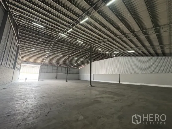 Warehouse for rent in Samut Prakan - View toward the main gate showing bright open-plan floor and steel roof structure.