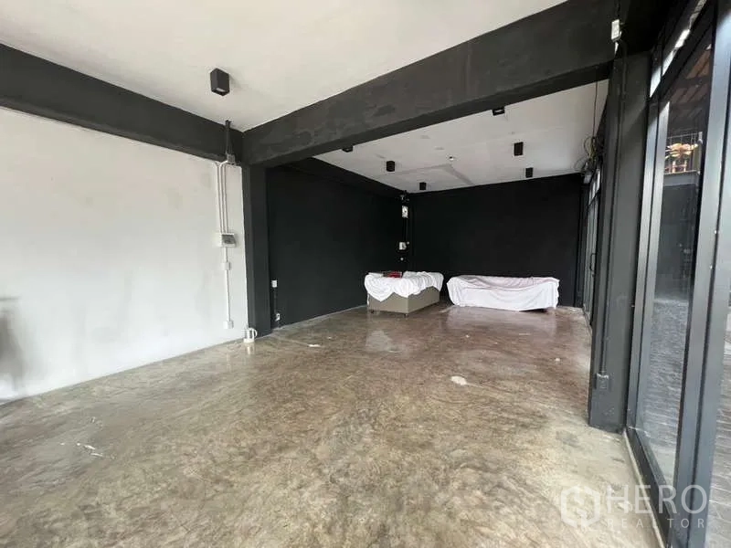 พื้นที่ขายปลีก ให้เช่า - ห้องโล่งทรงสี่เหลี่ยม ผนังขาวดำ ไฟเพดาน และหน้าร้านกระจกติดโถงทางเดิน