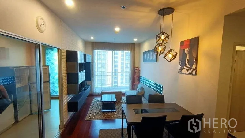 คอนโด ขาย - พื้นที่นั่งเล่นสว่าง มีชั้นทีวี ชุดทานอาหาร และประตูกระจกเปิดสู่ระเบียง