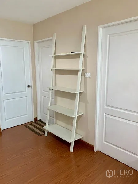 Condominium for rent in Huai Khwang, Bangkok - Entry corridor with white ladder bookcase and two paneled doors on wood flooring.