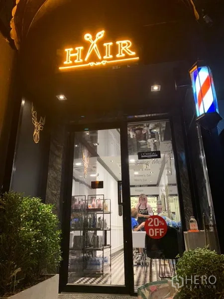 พื้นที่ขายปลีก ให้เช่าในWatthana, Bangkok - มุมมองตอนกลางคืนของหน้าร้านพร้อมป้ายไฟ HAIR ประตูบานกระจก เสาสัญลักษณ์บาร์เบอร์ และไม้พุ่มหน้าอาคาร