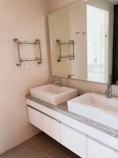 Condominium for rent or sale in Khlong Toei, Bangkok - Bathroom with double square basins on a stone countertop, large mirror and chrome fixtures in neutral tiles.