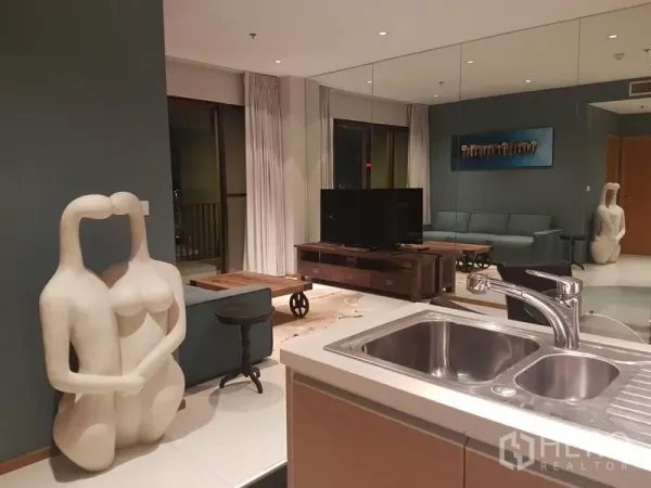 คอนโด ให้เช่าหรือขายในKhlong Toei, Bangkok - ห้องนั่งเล่นแบบโอเพนแพลน ผนังกระจกเงา ชุดทีวี และประตูกระจกออกสู่ระเบียง มองจากอ่างล้างจานในครัว