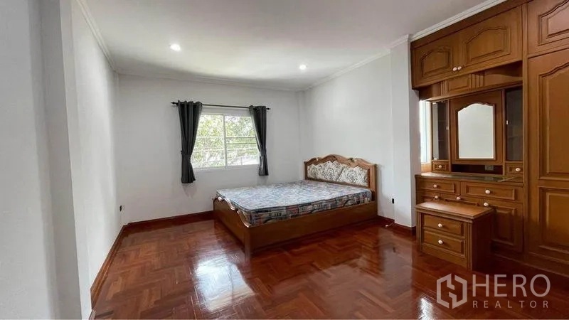 Detached House for rent in Bang Kapi, Bangkok - Large bedroom with window, curtains, wooden built-in wardrobe and parquet floors.