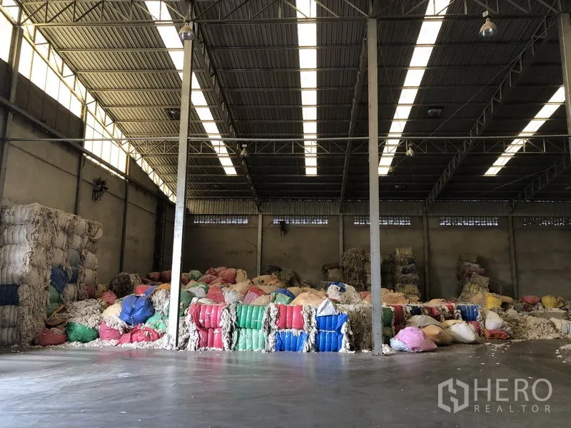 工厂 出租在Bang Bua Thong, Nonthaburi - 仓库纵深通道，条形天窗与两侧堆放的物料。