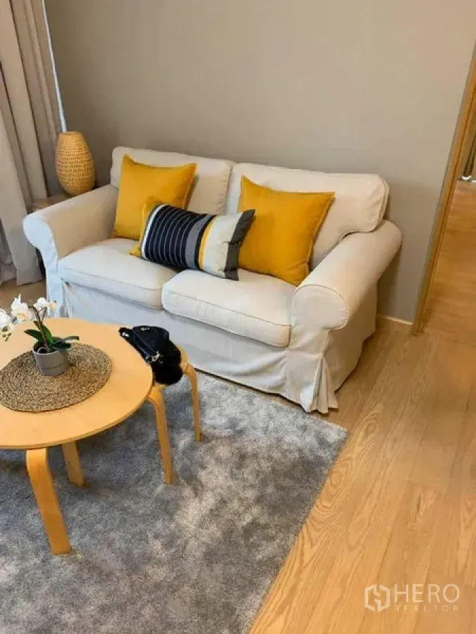 คอนโด ให้เช่าในWatthana, Bangkok - มุมนั่งเล่นกะทัดรัด โซฟาสีครีม หมอนสีเหลือง โต๊ะกาแฟไม้ทรงกลมและพรม