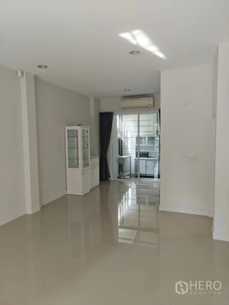 联排别墅 出租或出售在Lat Phrao, Bangkok - 宽敞客厅，通向玻璃隔断的厨房，配空调与高窗帘。