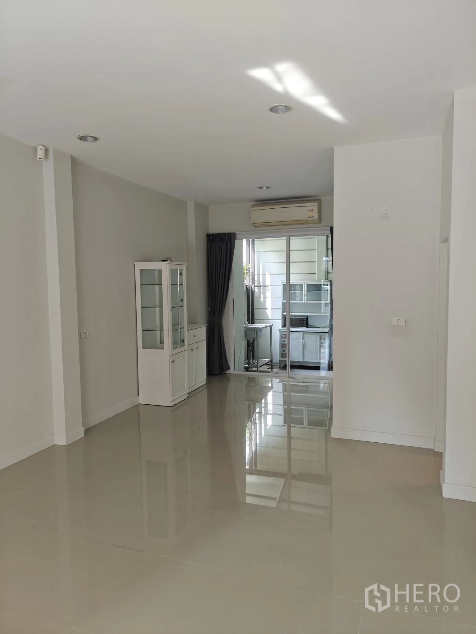 联排别墅 出租或出售在Lat Phrao, Bangkok - 宽敞客厅，通向玻璃隔断的厨房，配空调与高窗帘。