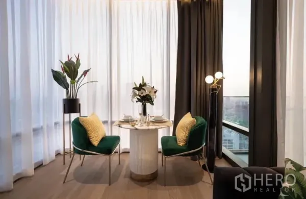 Condominium for rent in Bang Rak, Bangkok - Cozy dining nook beside full-height windows with a round table, green chairs and sheer curtains framing a city view.