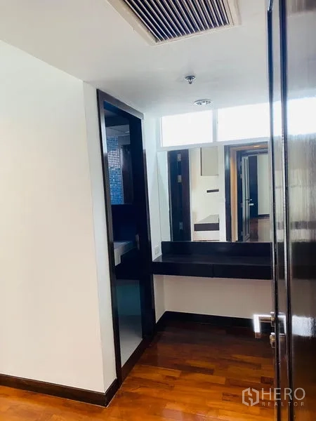 Condominium for rent in Watthana, Bangkok - Hallway nook with countertop and mirror next to the bathroom, set on polished wood floors.