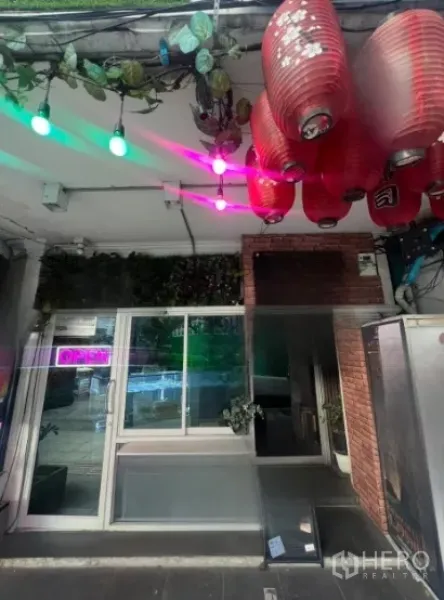 店屋 出租在Watthana, Bangkok - 临街店屋入口，玻璃推门、红色灯笼、霓虹OPEN招牌与绿植，靠近曼谷通罗站。