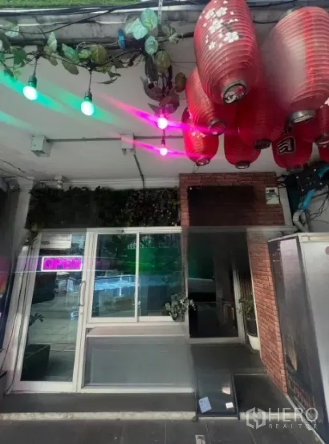 店屋 出租在Watthana, Bangkok - 临街店屋入口，玻璃推门、红色灯笼、霓虹OPEN招牌与绿植，靠近曼谷通罗站。