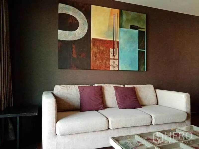 公寓 出租在Sathon, Bangkok - 温馨客厅，白色沙发、彩色挂画与玻璃面茶几。