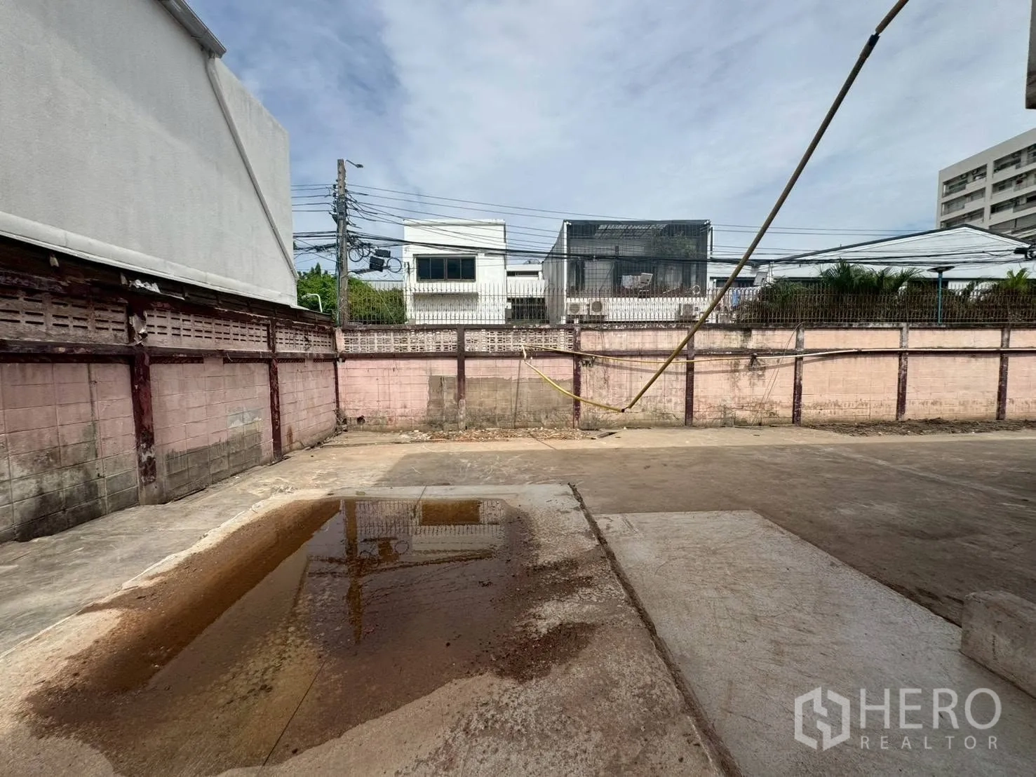 Detached House for rent or sale in Watthana, Bangkok - Walled concrete yard with a puddle and surrounding low-rise buildings.