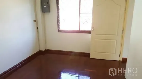 Detached House for rent in Khlong Toei, Bangkok - Empty room with polished wooden floor, cream door and a window with security grilles.