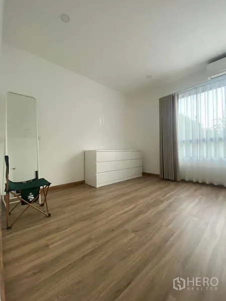 Townhouse for rent in Bang Kapi, Bangkok - Large room with chest of drawers, window, mirror and warm wood-look floor.