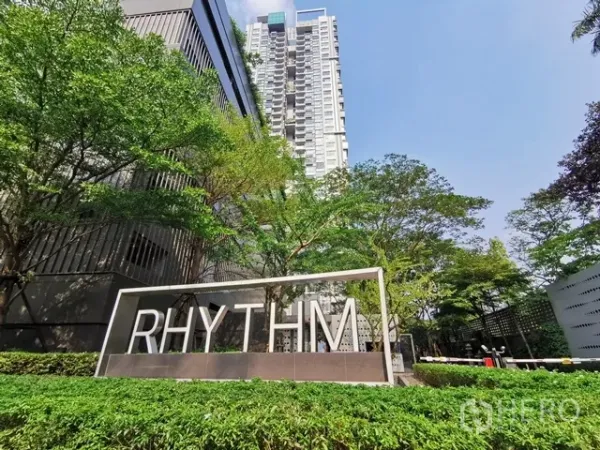 Condominium for rent in Khlong Toei, Bangkok - Condominium tower exterior with RHYTHM sign and landscaped entrance surrounded by trees.