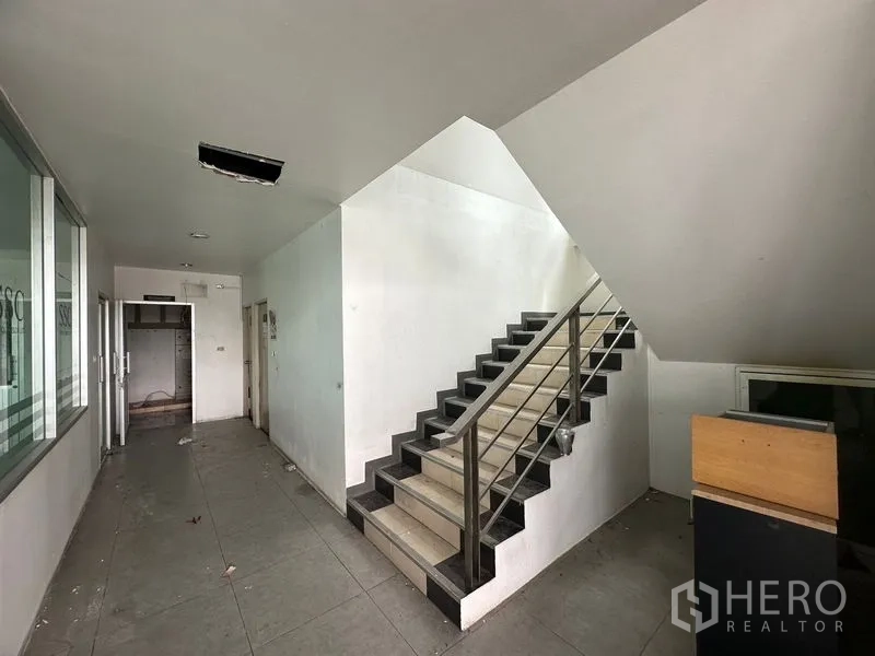 Showroom for rent or sale in Lam Luk Ka, Pathum Thani - Interior stairwell with metal handrail beside glass offices.