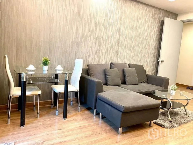 Condominium for rent in Huai Khwang, Bangkok - Dining nook beside sofa with glass table and two upholstered chairs.