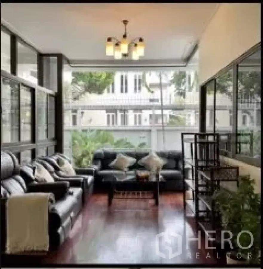 独立式住宅 出租在Phra Khanong, Bangkok - 封闭式阳台客厅，皮沙发与落地窗景。