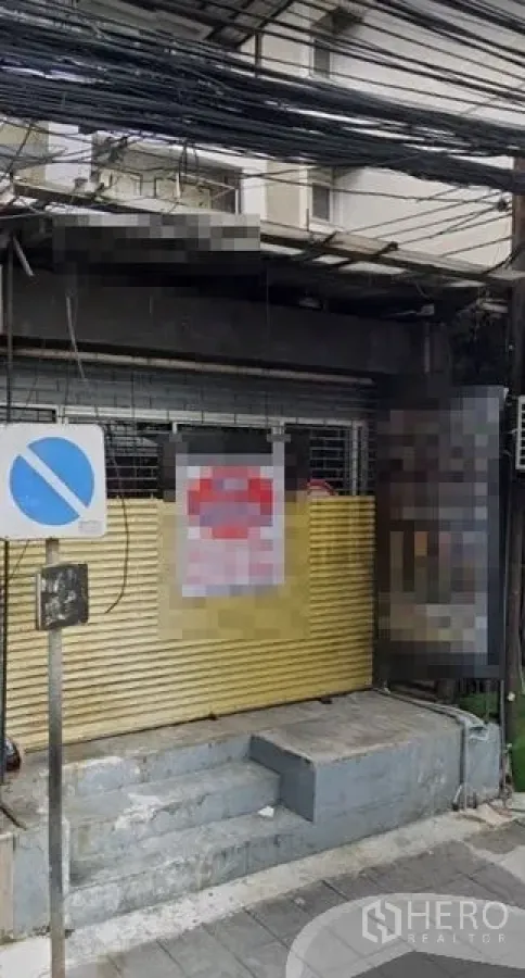 零售空间 出租在Din Daeng, Bangkok - 临街店铺外立面，金属卷闸门关闭，台阶入口、人行道与上方电缆，城市街景。