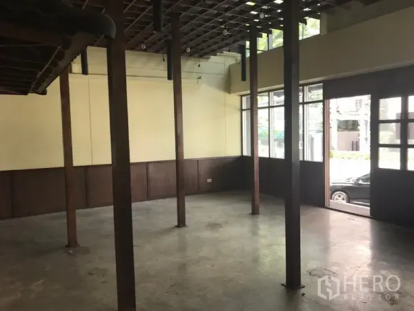 零售空间 出租在Khlong Toei, Bangkok - 开放式零售室内，木柱、混凝土地面、格栅吊顶与临街采光窗，靠近BTS通罗站