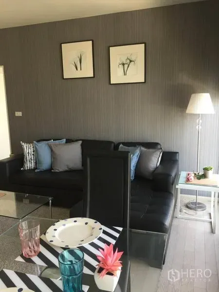 Condominium for rent in Watthana, Bangkok - Open-plan living and dining area with leather sectional, framed art, floor lamp, and table setting.