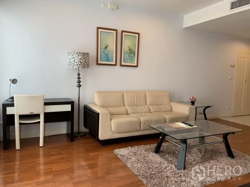 คอนโด ให้เช่าในKhlong Toei, Bangkok - มุมนั่งเล่นมีโซฟาสีครีม โต๊ะทำงาน โคมไฟยืน และโต๊ะกลางกระจกบนพรม