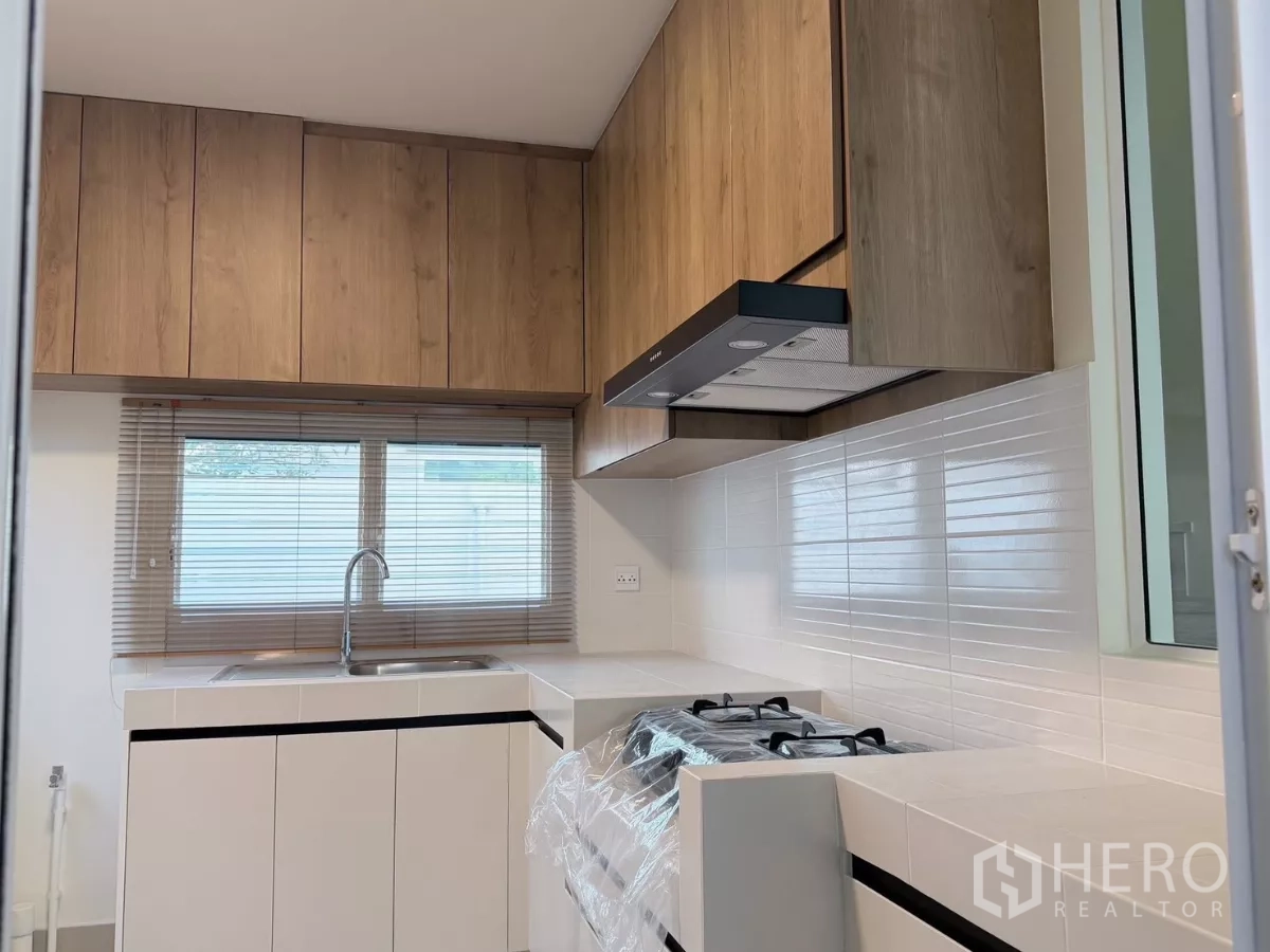 Detached House for rent in Bang Phli, Samut Prakan - Separate kitchen with wood cabinetry, gas hob, range hood and white countertops.