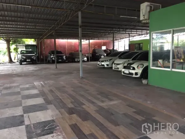 Warehouse for rent in Pathum Thani - Sheltered warehouse parking area with tiled floor beside a green office unit.