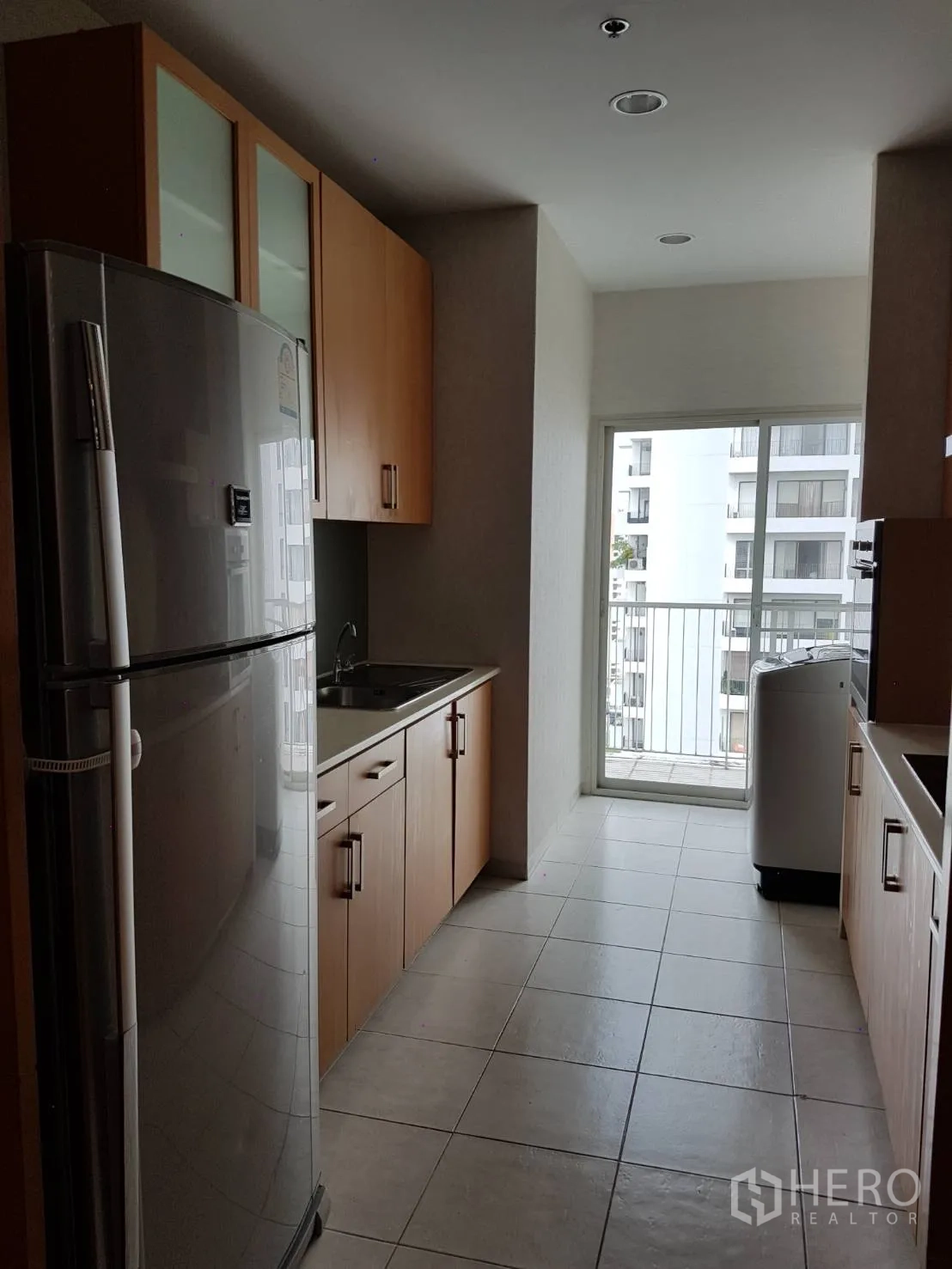 Condominium for rent or sale in Watthana, Bangkok - Opposite side of the kitchen showing double-door fridge, sink, and access to a small balcony.