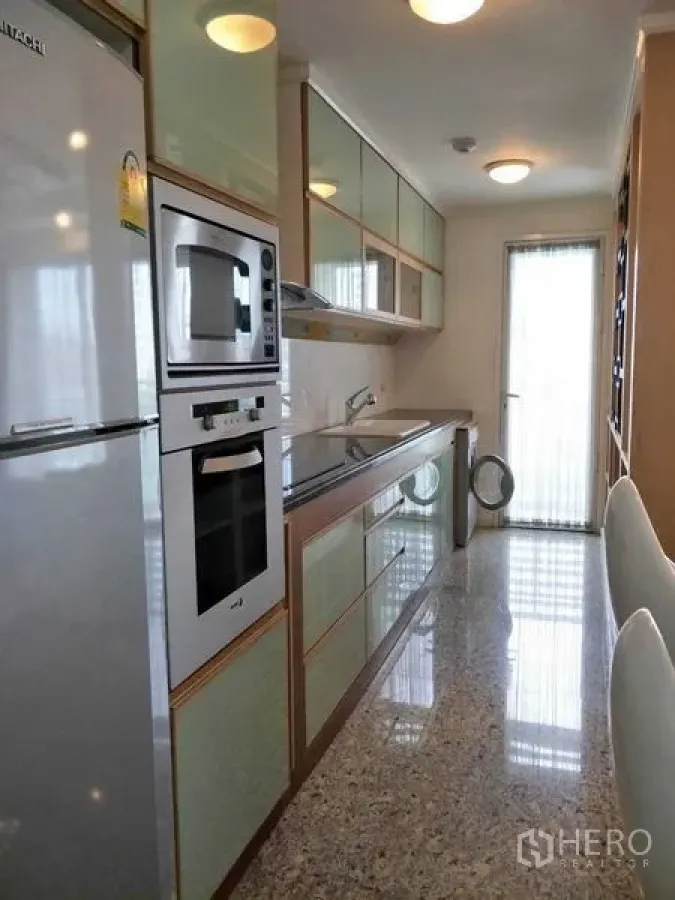 คอนโด ให้เช่าหรือขายในWatthana, Bangkok - ครัวแบบแกลลีย์ ตู้กระจกสีมิ้นท์ เตาอบบิวท์อินและประตูระเบียง ในคอนโดเอกมัย เขตวัฒนา