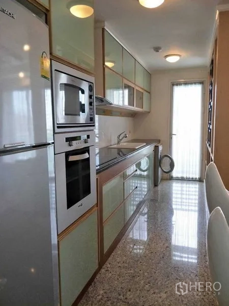 คอนโด ให้เช่าหรือขายในWatthana, Bangkok - ครัวแบบแกลลีย์ ตู้กระจกสีมิ้นท์ เตาอบบิวท์อินและประตูระเบียง ในคอนโดเอกมัย เขตวัฒนา