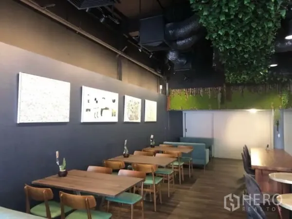 店屋 出租在Ratchathewi, Bangkok - 用餐区视角，成排木桌与绿色坐垫椅，高挑深色天花配藤蔓装饰与墙面艺术，店屋呈咖啡馆氛围。