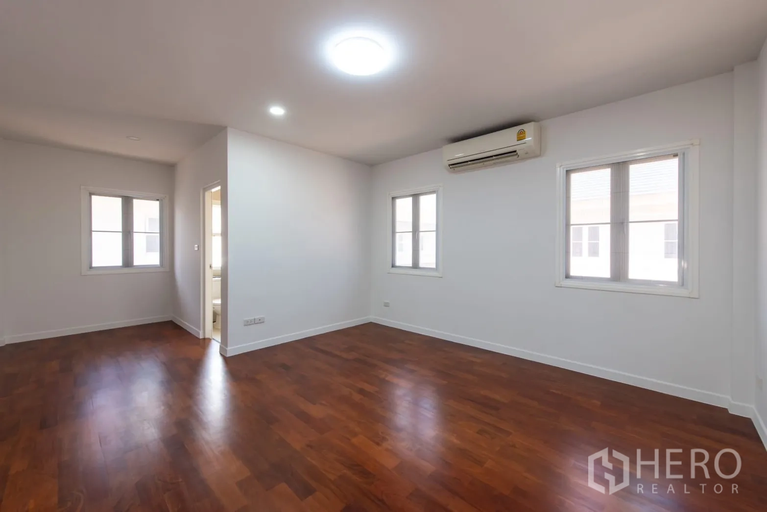Detached House for sale in Bang Phli, Samut Prakan - Large bedroom with ensuite door, windows, wooden floor and air conditioner.