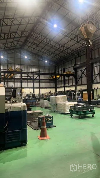 工厂 出售在Si Racha, Chon Buri - 傍晚车间视角，显示起重葫芦、设备与托盘。