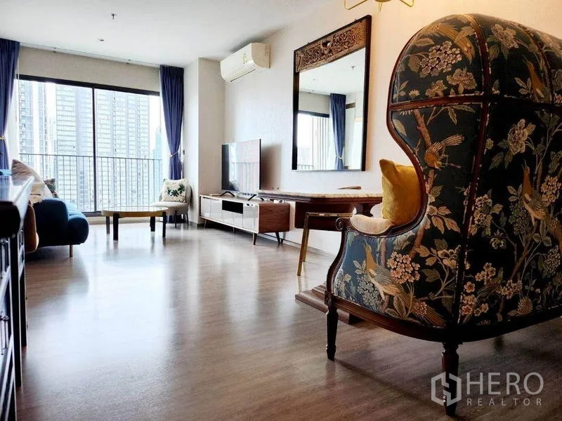 คอนโด ให้เช่าในWatthana, Bangkok - มุมห้องนั่งเล่นที่มีเก้าอี้วิงแบ็กลายผ้า ชุดวางทีวี และหน้าต่างบานใหญ่เชื่อมระเบียง