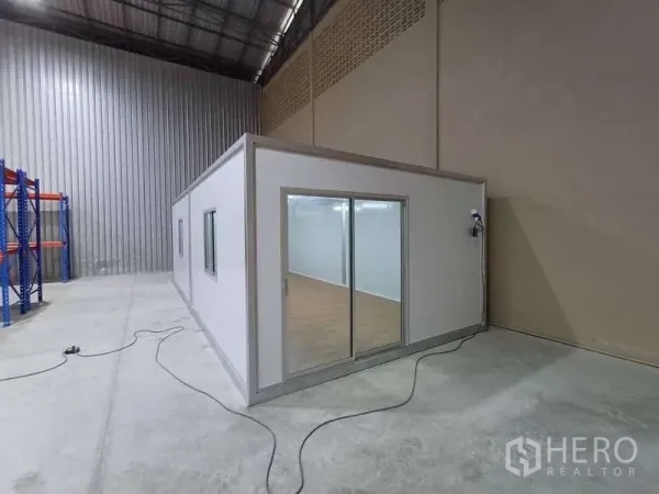 Warehouse for rent in Rat Burana, Bangkok - Modular office unit with glass sliding doors built inside the warehouse beside a tall corrugated wall.