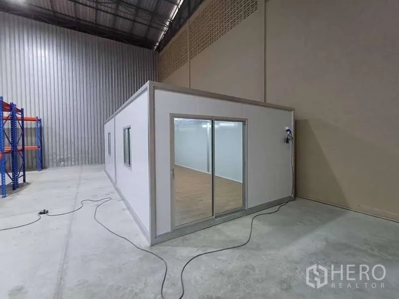 Warehouse for rent in Rat Burana, Bangkok - Modular office unit with glass sliding doors built inside the warehouse beside a tall corrugated wall.