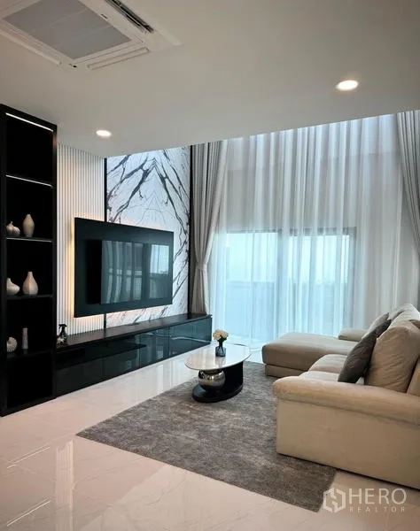 Detached House for rent or sale in Bang Phli, Samut Prakan - Living room with marble TV wall, built-in shelving, and floor-to-ceiling drapes.